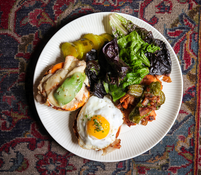 A plate of huevos rancheros with a sunny-side-up egg, green salsa roja, and a side of mixed greens on a patterned tablecloth.
