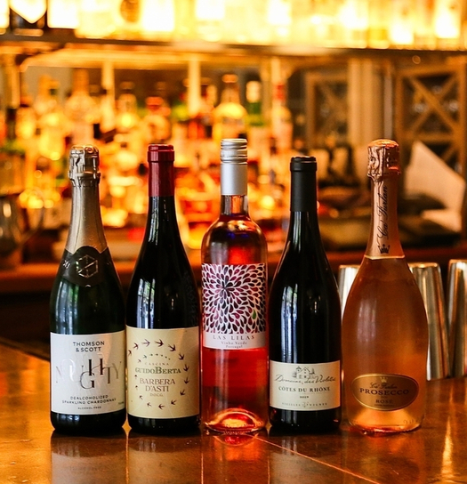 A row of five wine bottles on a bar counter, featuring various labels and colors.背景模糊，显示酒柜。