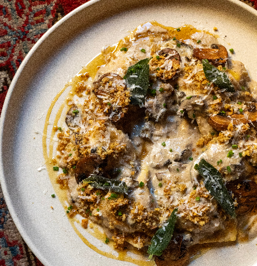Plated pasta dish with golden breadcrumbs, sautéed greens, and grated cheese in a cream sauce on a white bowl.