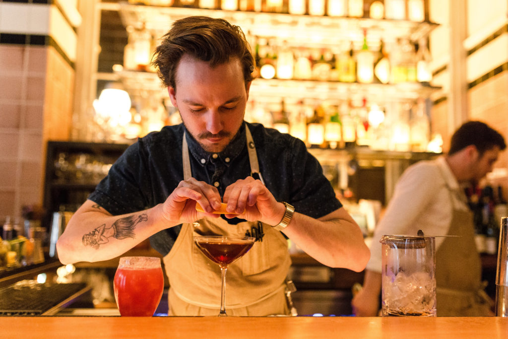 Bartender squeezing an orange peel into a cocktail at the bar